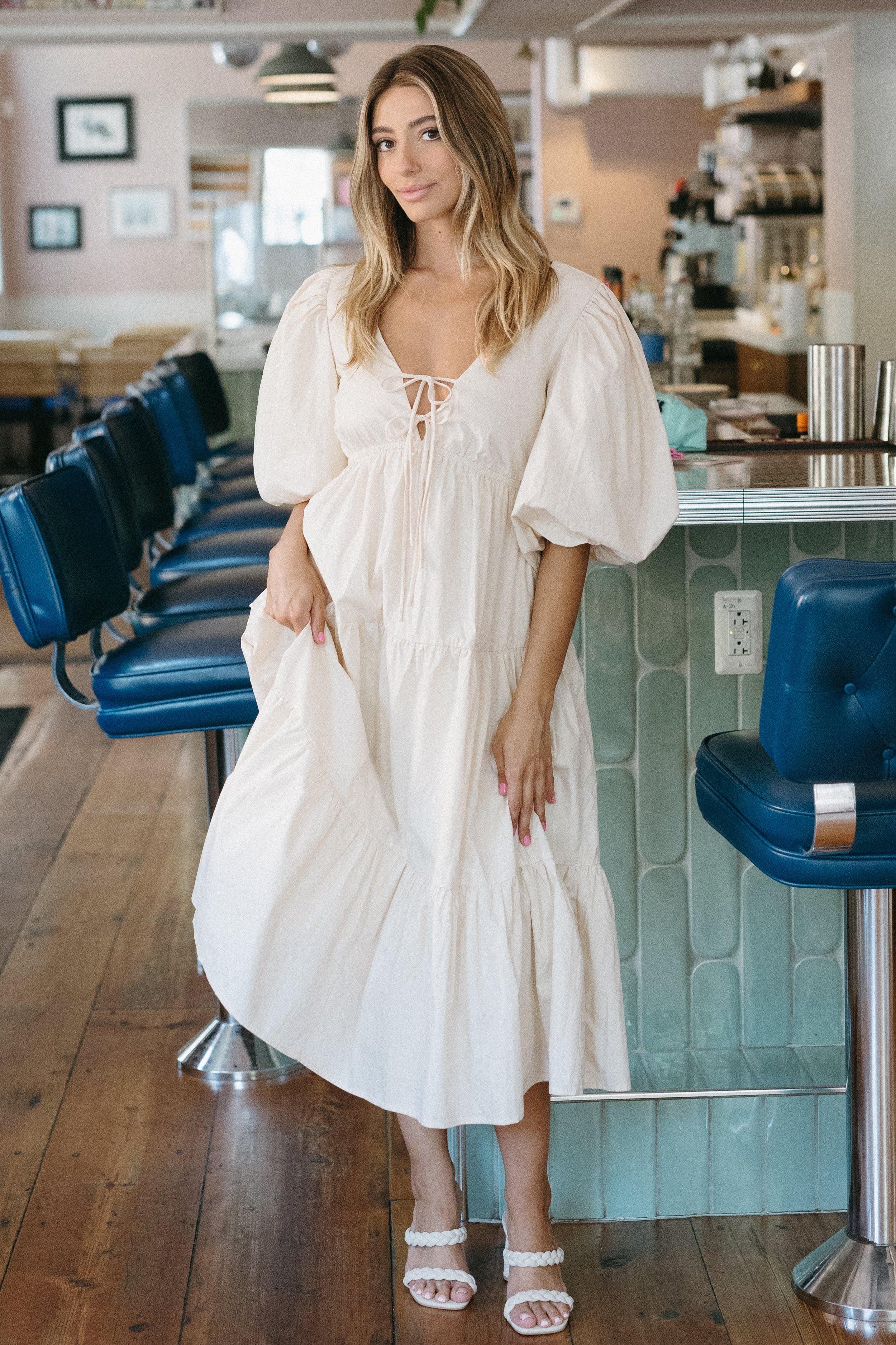 Woman in a white dress standing in a modern cafe with blue chairs and a 'Summer Bubbly' sign.