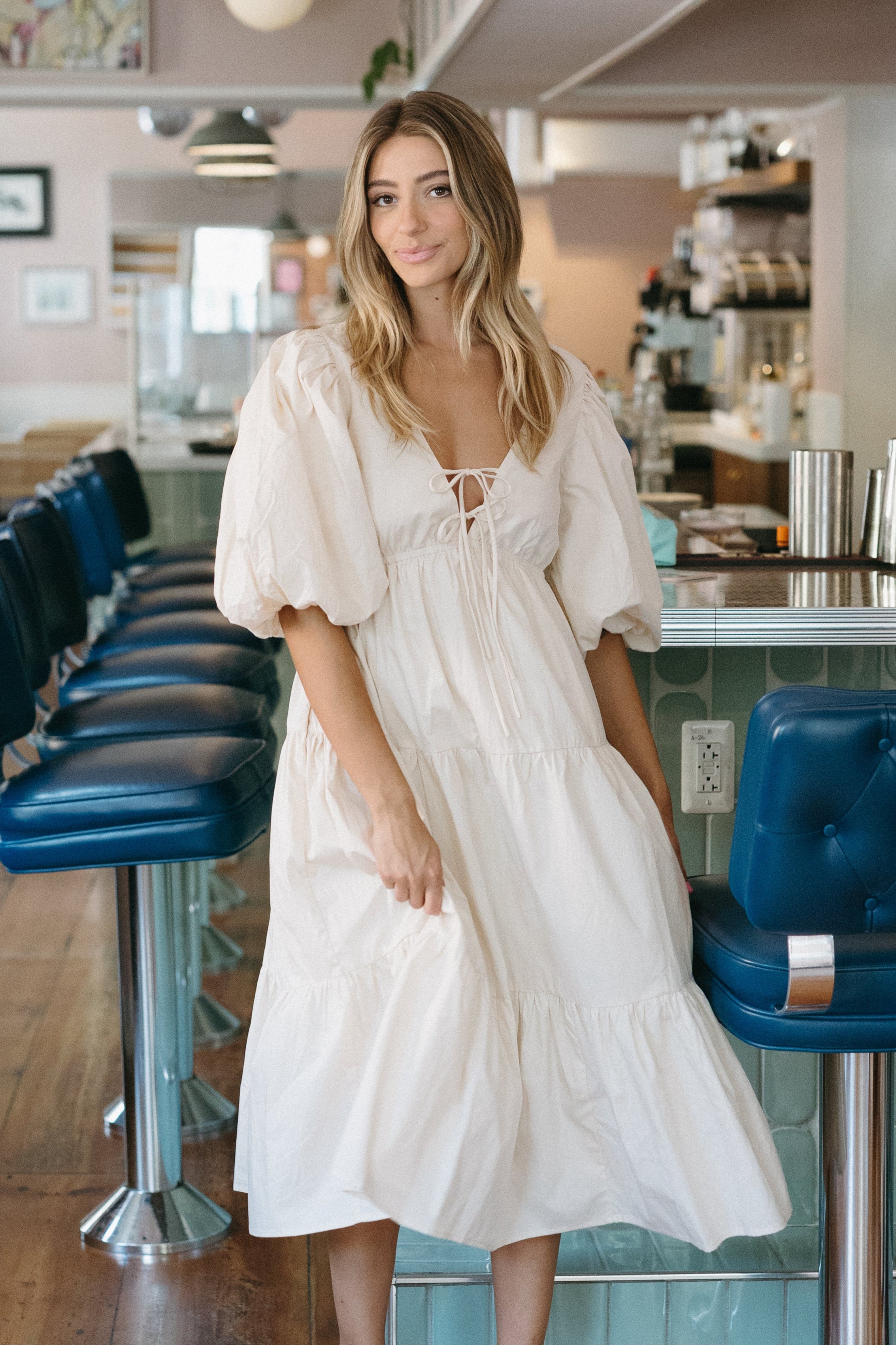 Woman in a white dress standing in a cafe with blue chairs and a 'Summer Bubbly' text overlay.