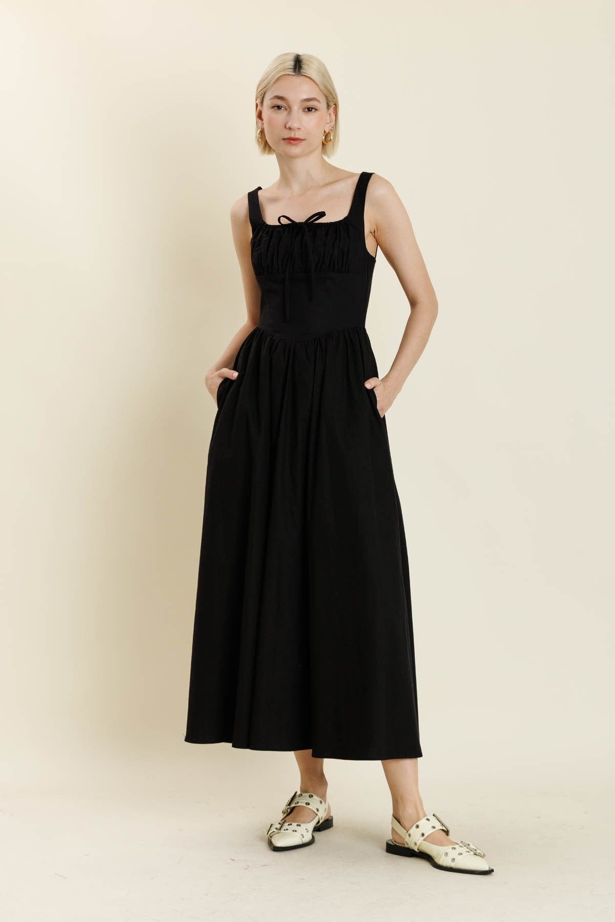 Woman wearing a black sleeveless dress against a beige background