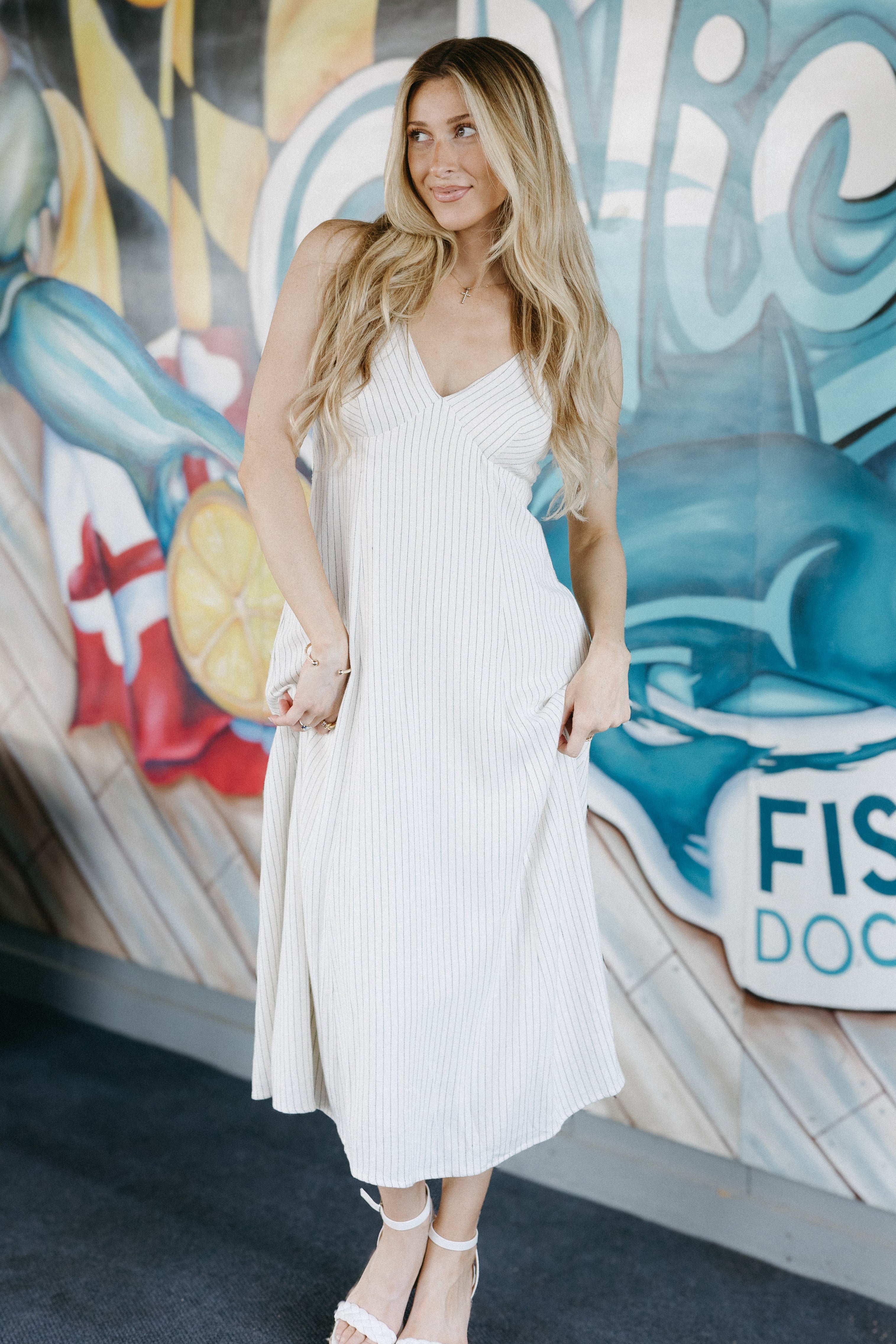 Woman in a white dress standing in front of a colorful mural with 'Fish Dock' text.