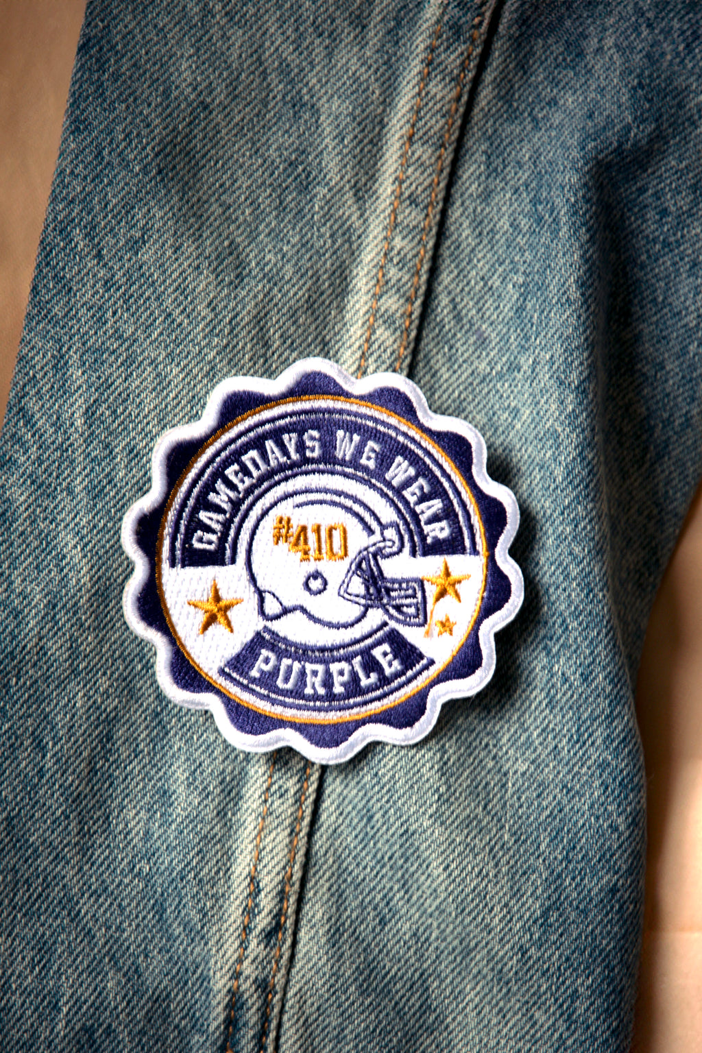 A purple patch with the text 'Game Days We Wear Purple' and a graphic of a football helmet on a denim jacket.