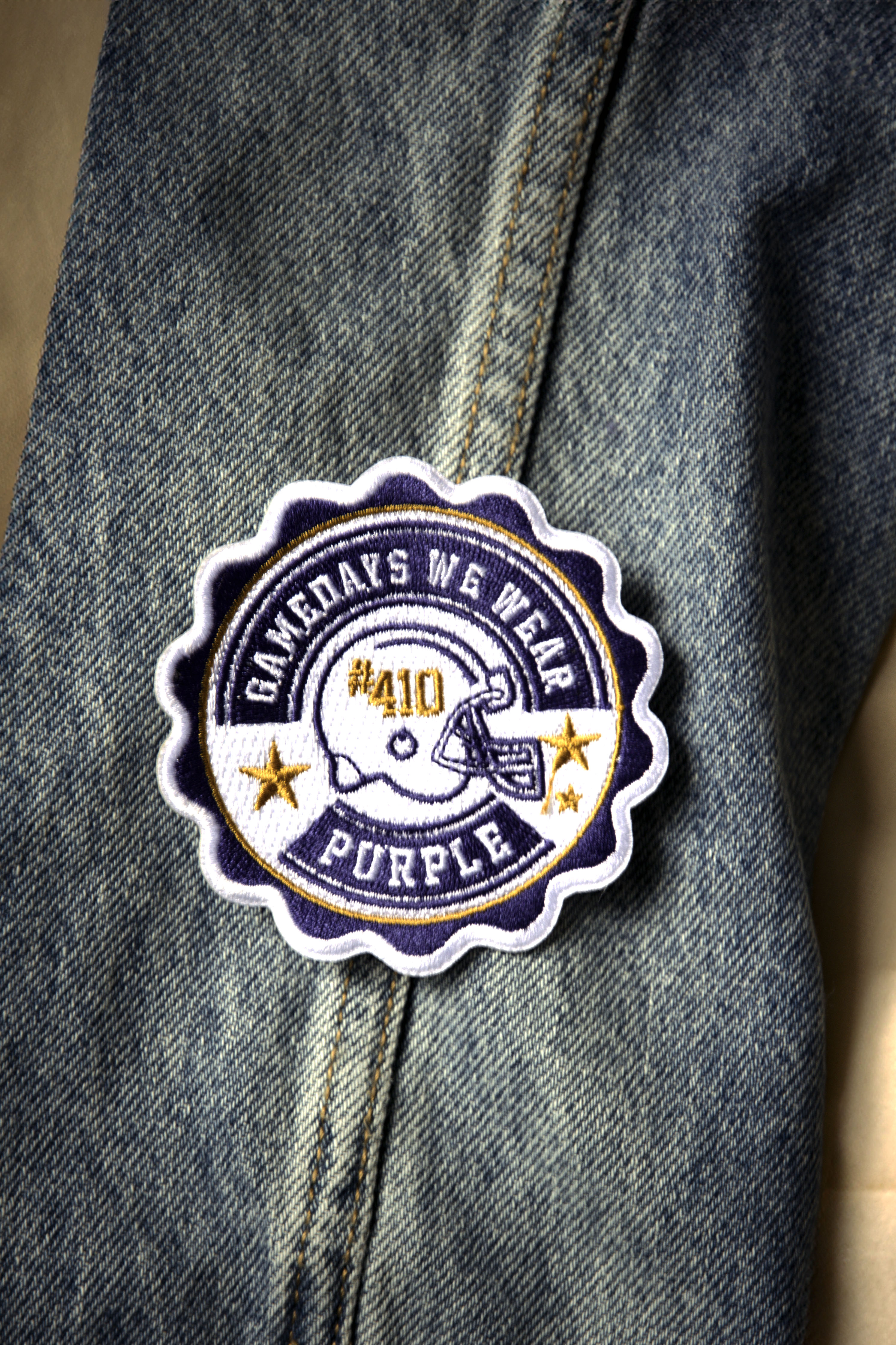 A purple patch with the text 'Game Days We Wear Purple' and a graphic of a football helmet on a denim jacket.