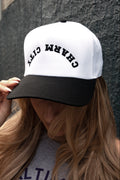 Person wearing a white cap with 'CHARM CITY' text against a gray wall.