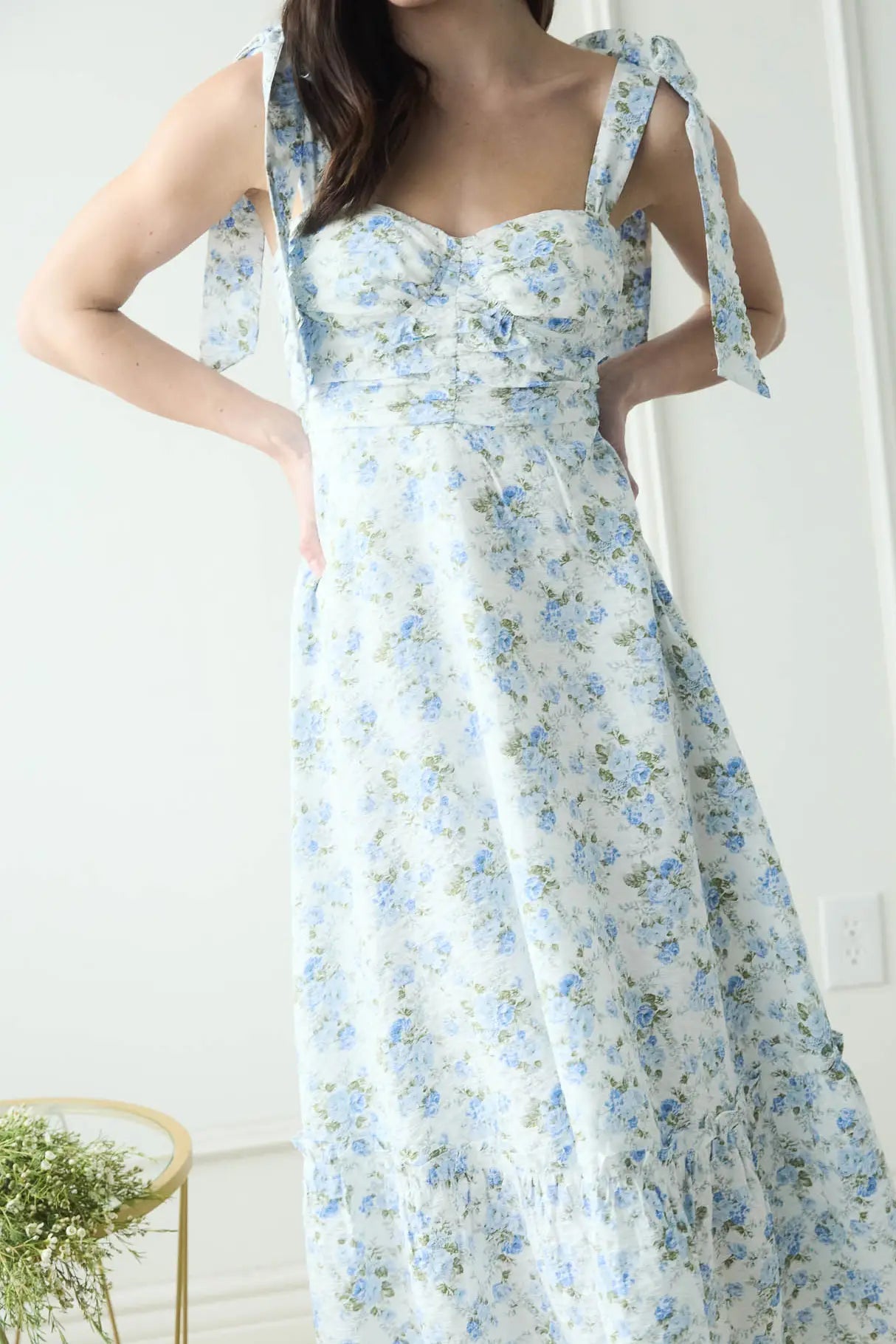 Woman wearing a floral dress with blue and white flowers in a minimal setting.