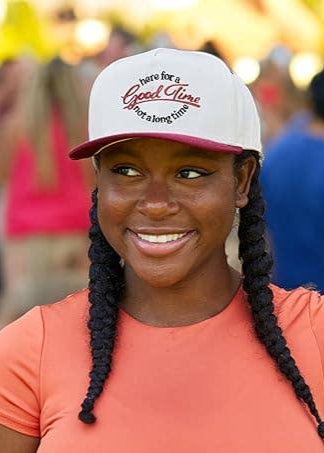 Woman wearing a cap with text, standing in a crowd with a blurred background